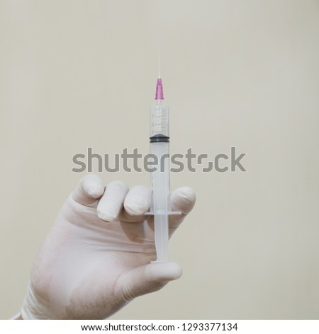 Syringe in hand doctor on white wall background.