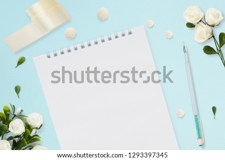 Styled stock photo. Feminine wedding desktop mockup. Greeting card. White roses, notebook, pen, tape on delicate blue background. Copy space. Top view. Picture for blog