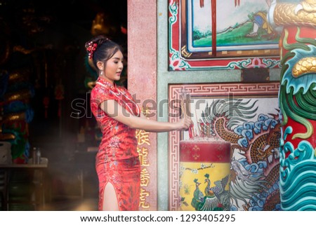 Concept to celebrate Chinese New Year : Chinese woman in a red cheongsam dress holding incense pay homage to Chinese god at shrine.