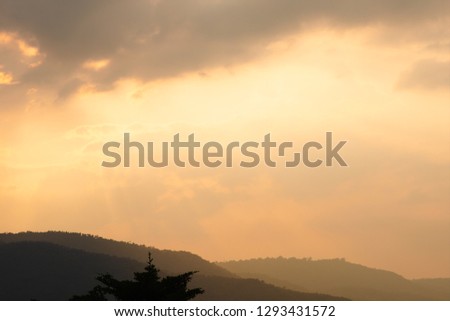 Sunset and beautiful twilight fluffy storm cloudy blue and yellow sky smoothly flowing pass the mountain forest. Rainny good evening and have a nice day concept.