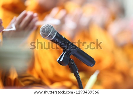 The buddhist monks are making a prayer together by using the black microphone with blurred and orange background, in concept of technology, audio, religion, faith, peaceful.
