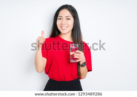 Young brunette woman drinking a glass of water over isolated background happy with big smile doing ok sign, thumb up with fingers, excellent sign