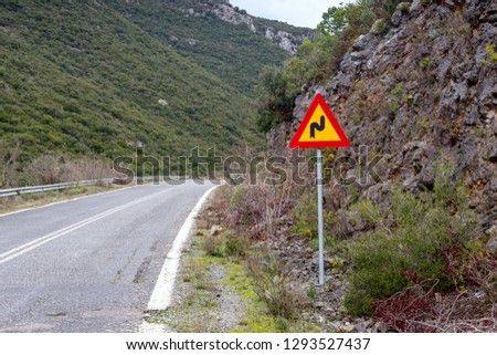 Sign "Dangerous turns with the first turn to the right" on a narrow mountain, rural road on a cloudy, winter day