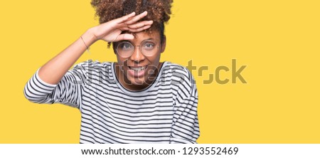 Beautiful young african american woman wearing glasses over isolated background very happy and smiling looking far away with hand over head. Searching concept.