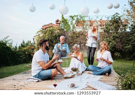 Family gathered outdoors, talking, laughing eating cake, celebrating  Royalty-Free Stock Photo #1293553927
