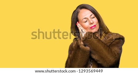 Beautiful middle age elegant woman wearing mink coat sleeping tired dreaming and posing with hands together while smiling with closed eyes.