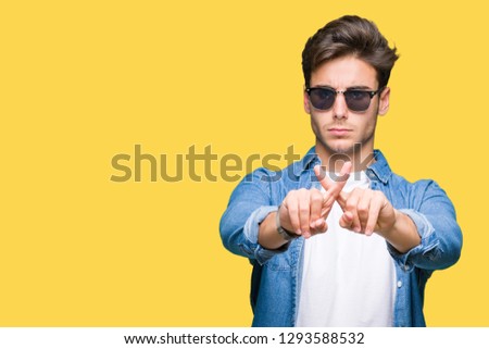Young handsome man wearing sunglasses over isolated background Rejection expression crossing fingers doing negative sign