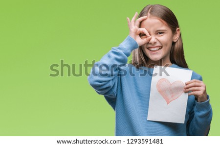 Young beautiful girl giving mother father day card with red heart over isolated background with happy face smiling doing ok sign with hand on eye looking through fingers
