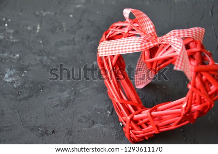 a red heart made of wood texture. A celebration of love. Valentine's day. wicker red heart with bow and ribbon on black background