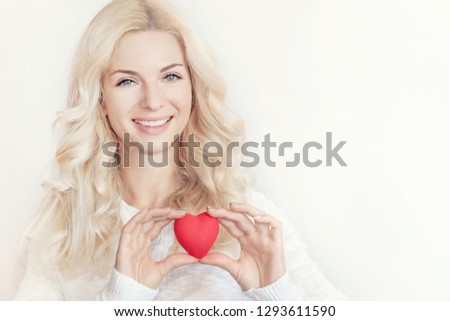 Happy smiling young blond woman holding red heart on white background. Love concept
