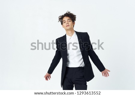 Cute elegant man in a black suit spreads his arms against a light background