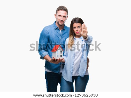 Young couple in love holding house over isolated background with open hand doing stop sign with serious and confident expression, defense gesture