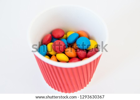 multicolored round candy dragee lie in a paper red glass