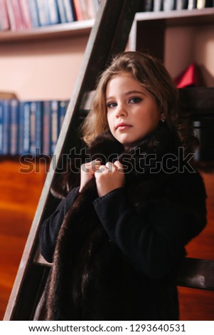 Little girl stand by the ladder in the library. Books