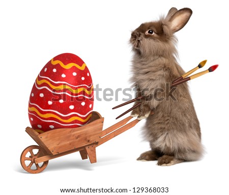 Cute Easter bunny rabbit with a little wheelbarrow and a red painted Easter egg, isolated on white, CG+photo