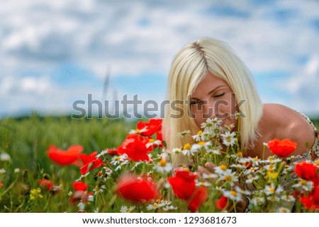 A beautiful, attractive, blond woman collects meadow flowers on the edge of the field. Soft focus.