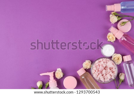 cosmetics for face and body in pink bottles with fresh roses on a bright purple background. cream and lotion, sea salt and soap. spa. view from above. space for text