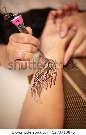 the master draws a mehendi in the form of a bird feather on his hand with black gel