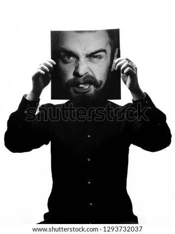 Black and white photo of man in the black shirt holding a photo with the face of a man with a beard in place of his face. Multiexposure
