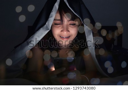 Portrait of smiling woman with mobile phone on bed in dark room.Abstract bokeh background.