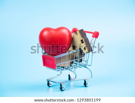 Red heart and wooden homes in shopping cart isolated on blue pastel background,health and family concept