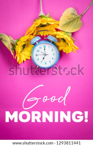 Beautiful retro blue pastel alarm clock on a vibrant pink background with sunflowers and quote Good morning