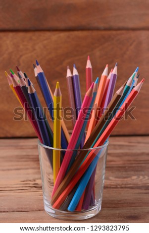 a set of colored pencils in a glass against the background of a wooden surface