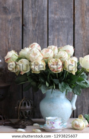 Bouquet of roses in old aged weathered clay pitcher, antique string twine holder, porcelain tea cup, on wooden background, vintage style