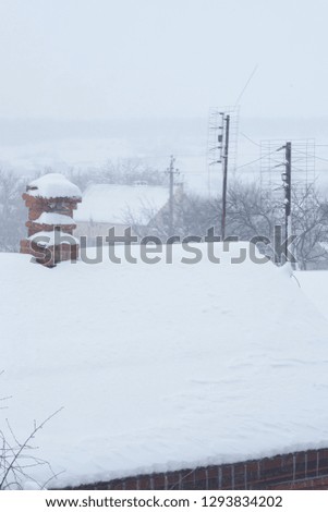 Chimney in red bricks and two antennas with white snow on roof.