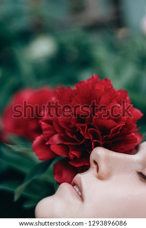  Beautiful and gentle portrait of a girl with eyes closed among the red flowers peonies.  Spring blossom
