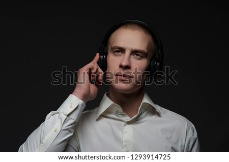 Young male music lover listens to music on headphones while working while posing on a black background. Creative music concept.