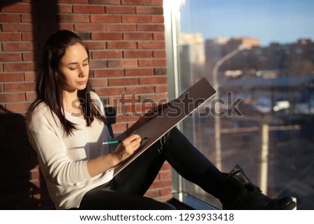 girl designer sitting on a chair by the window and draws a sketch works as an artist
