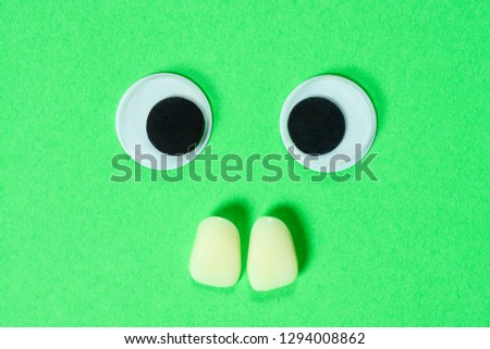Mad googly eyes with two yellow teeth on neon green background, cross-eyed funny toys eyes close-up.