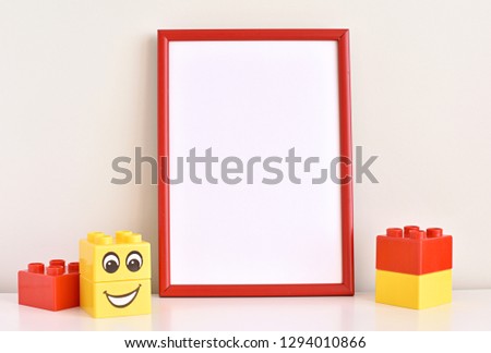 Nursery or kids room red empty frame mock up, plastic toy bricks with smiling face.