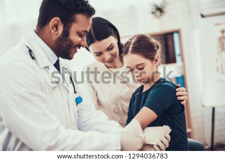 Indian doctor in white gown seeing patients in office. Doctor is using harness on daughter's arm.