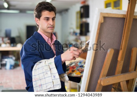 Creative male artist drawing picture with oil paints in studio