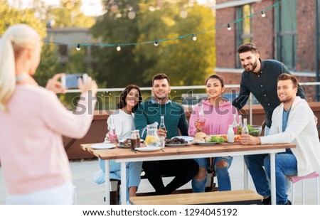 leisure and people concept - happy friends with non alcoholic drinks having dinner party on rooftop in summer and photographing by smartphone