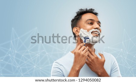 grooming and people concept - young indian man shaving beard with manual razor blade over blue background with low poly shape projection
