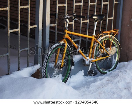 The bike is chained to the gate grille. Winter time, snow everywhere. The picture was taken in the morning, the bike is not in the snow. So someone drives on bicycle to work, or home.