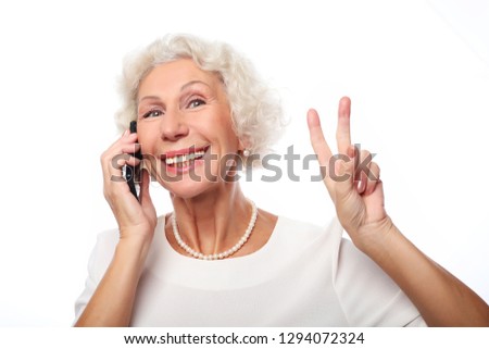 lifestyle, tehnology  and people concept: Elderly lady holding  a smartphone and making v-sign 