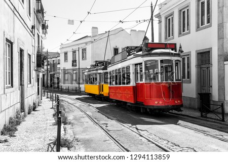 Yellow and red vintage tram on old streets of Lisbon, Alfama, Portugal, popular touristic attraction and destination. Black and white picture with a coloured tram.