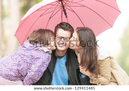Young family of three having fun outdoor. Pretty little daughter, beautiful wife and mother kissing their father and husband under pink umbrella. Portrait of happy and friendly family.