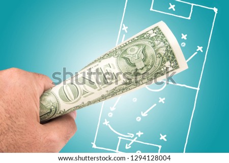 a white man holding dollar banknote with the picture of soccer footbal filed with play tactics and strategy drawn on light blue background