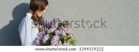 Young teen girl with bouquet of lilac near gray wall outdoor background, panoramic banner, girl in profile, copy space