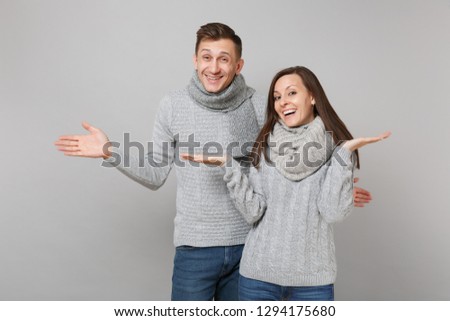 Young cute couple girl guy in gray sweaters, scarves together isolated on grey wall background, studio portrait. Healthy lifestyle, ill sick disease treatment, cold season concept. Mock up copy space