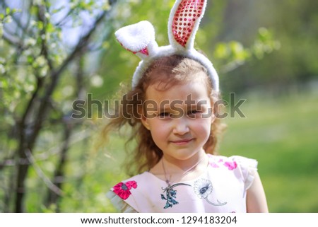 Cute little child wearing bunny ears on easter day. Beautiful curly-haired girl on background of flowering gardens in spring.