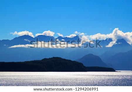 The afternoon sun glittering across the waters of Lake Manapouri in the South Island of New Zealand, with the Southern Alps in silhouette and shrouded in cloud.