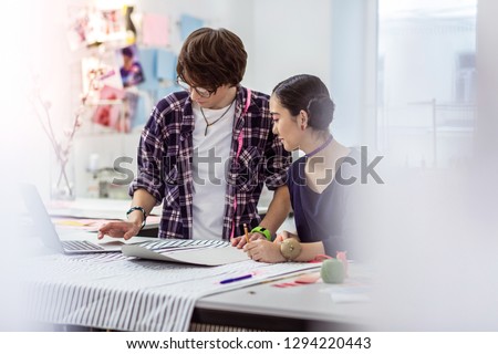 Dress pattern. Young male asian designer with piercing wearing a checkered shirt looking serious while preparing a dress pattern