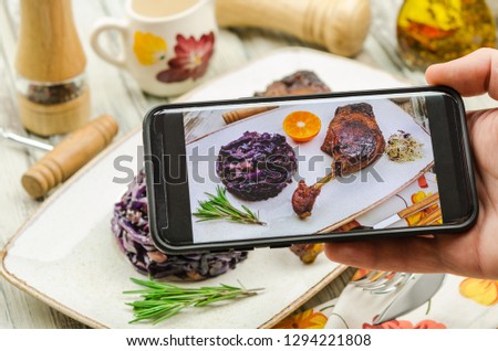 Young man taking photo of roasted duck leg dish on smartphone. Taking food photo with mobile phone.