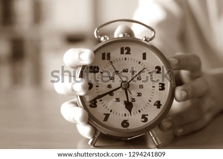 Black and white images of hands holding a red alarm clock on the table in the reading room